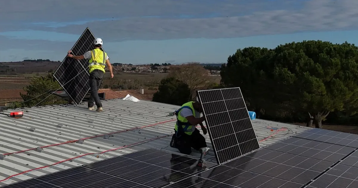 Deux techniciens SmartSun posant des modules photovoltaïques sur une grande toiture bac acier